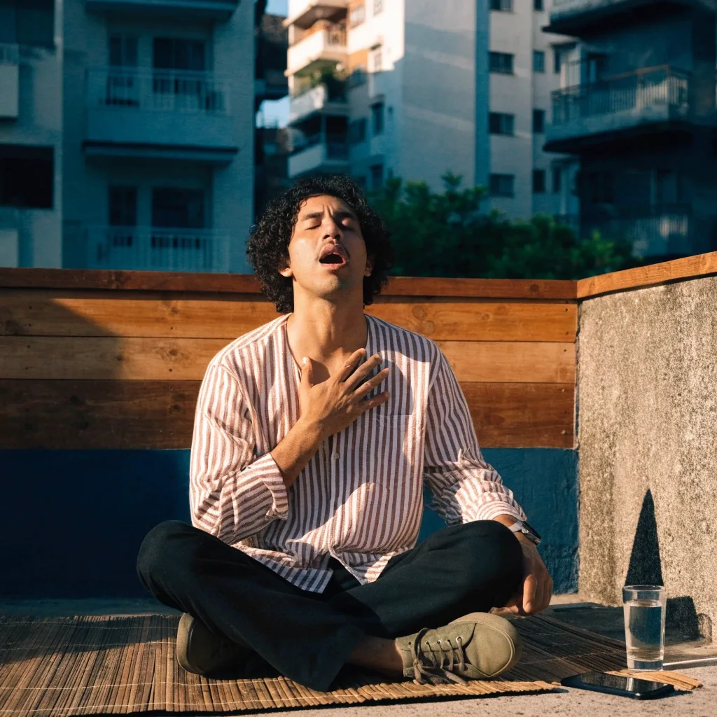 A man sitting on a sunlit Jakarta balcony with a phone resting face-down beside him